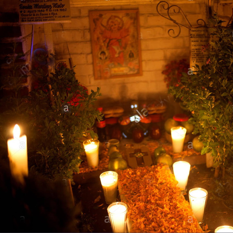 a-boy-sits-in-a-tomb-decorated-with-candles-and-yellow-marigold-flowers-FE5P1R
